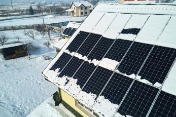 Luftaufnahme der Schneeschmelze von abgedeckten photovoltaischen Solarmodulen, die auf dem Dach eines Hauses installiert sind, um saubere elektrische Energie zu erzeugen