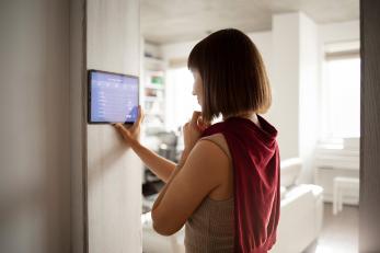 Eine Frau steuert ihr Smart Home per Tablet, das an der Wand angebracht ist