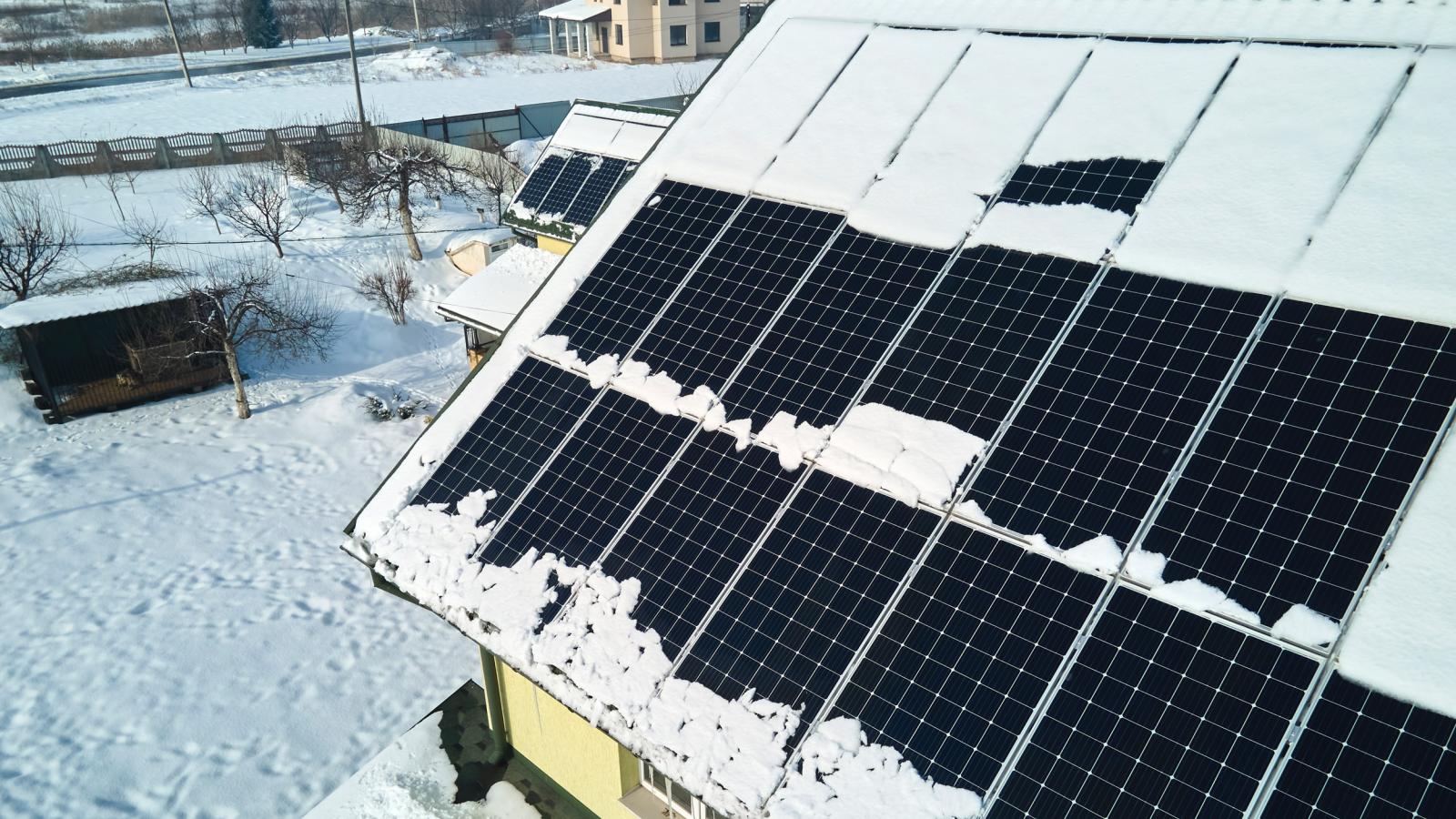 Luftaufnahme der Schneeschmelze von abgedeckten photovoltaischen Solarmodulen, die auf dem Dach eines Hauses installiert sind, um saubere elektrische Energie zu erzeugen