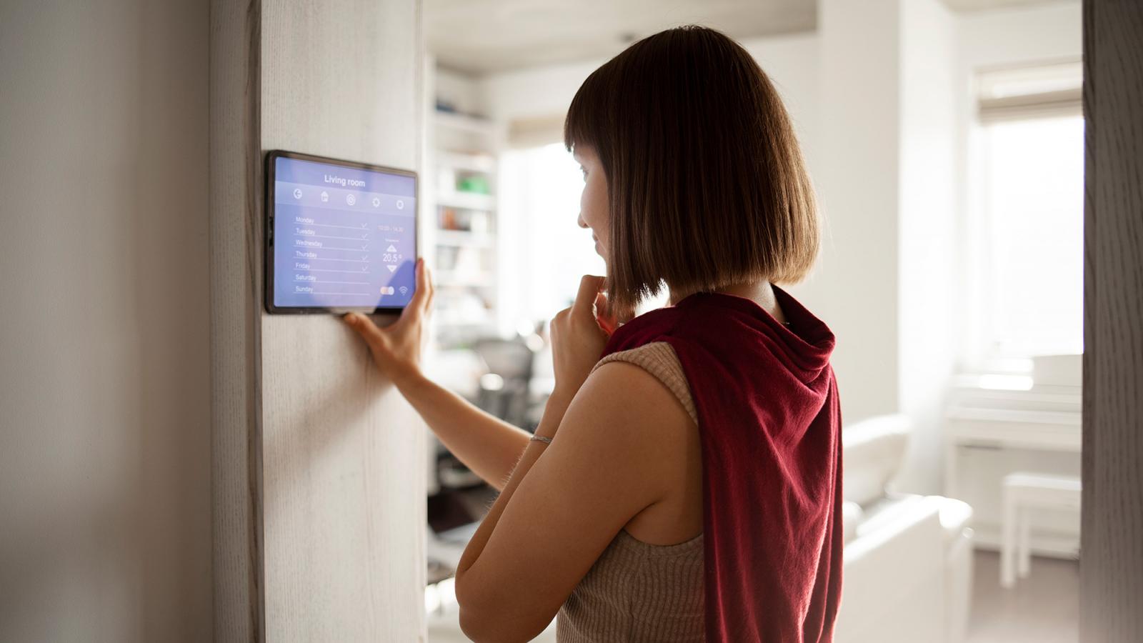 Eine Frau steuert ihr Smart Home per Tablet, das an der Wand angebracht ist